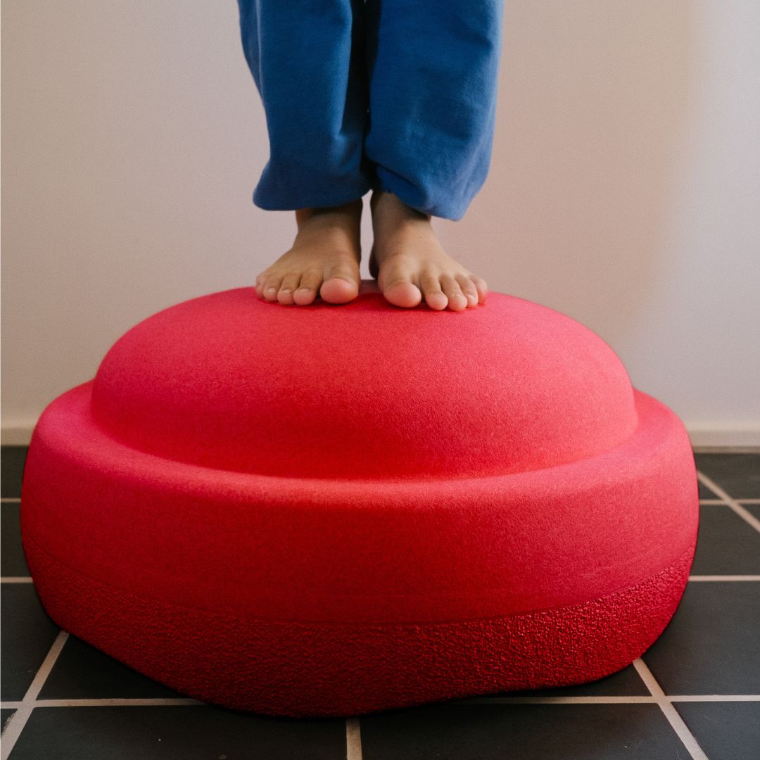 Blote voeten staan op een rood stapelstein schuimrubberblok op een tegelvloer.