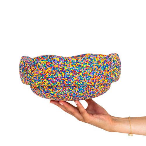 Een hand houdt een veelkleurig, gespikkeld stapelstein speelelement vast.