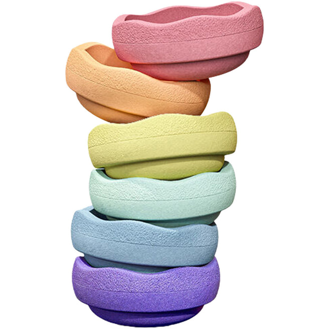 Zes gestapelde stapelstein balansstenen in pastel regenboogkleuren, schuin van bovenaf gezien.