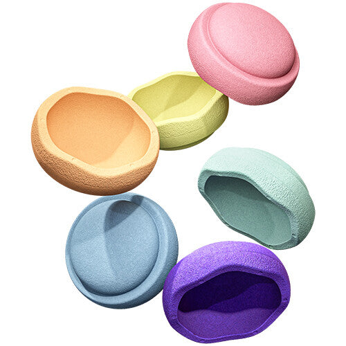 Zes losse stapelstein balansstenen in pastel regenboogkleuren, verspreid over de vloer.