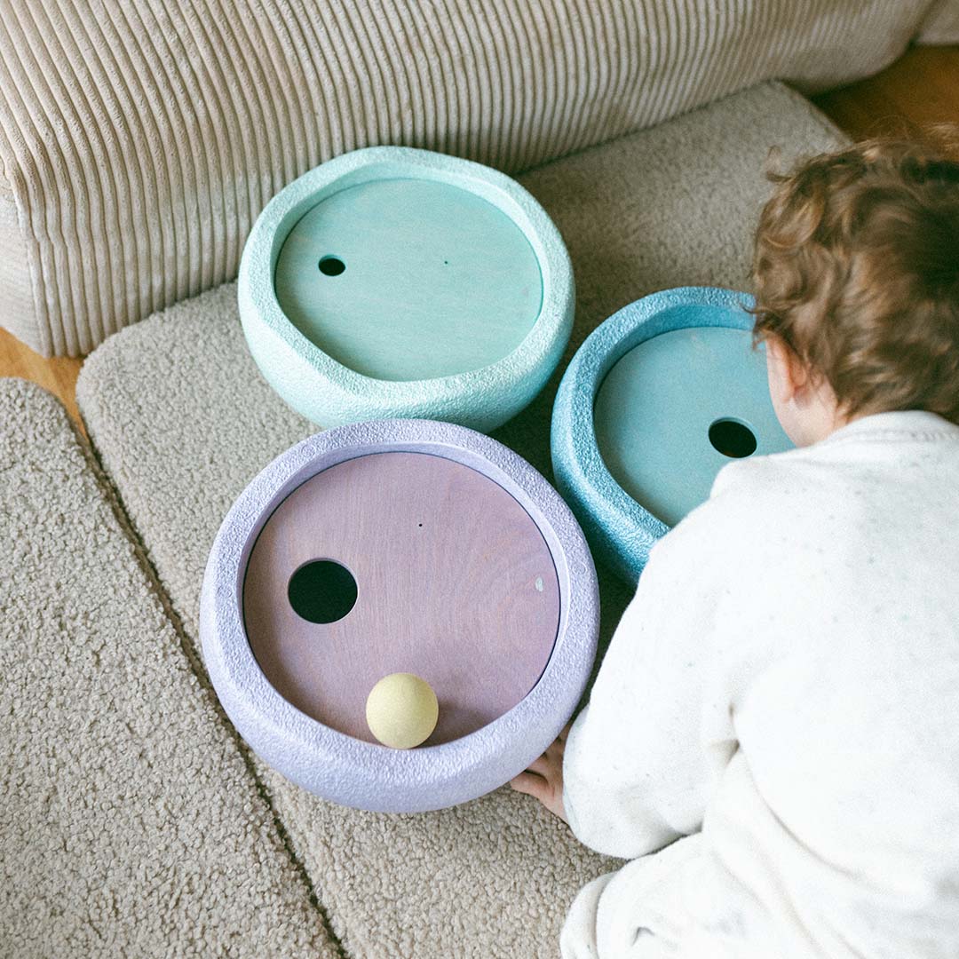 Een kind speelt met drie pastelkleurige stapelstein rolling discs op een vloerkleed.