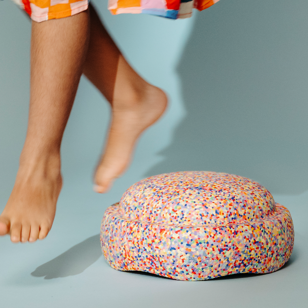 Stapelstein schuimrubberblok met confetti patroon op een blauwe vloer, met blote kindervoeten die erboven zweven.