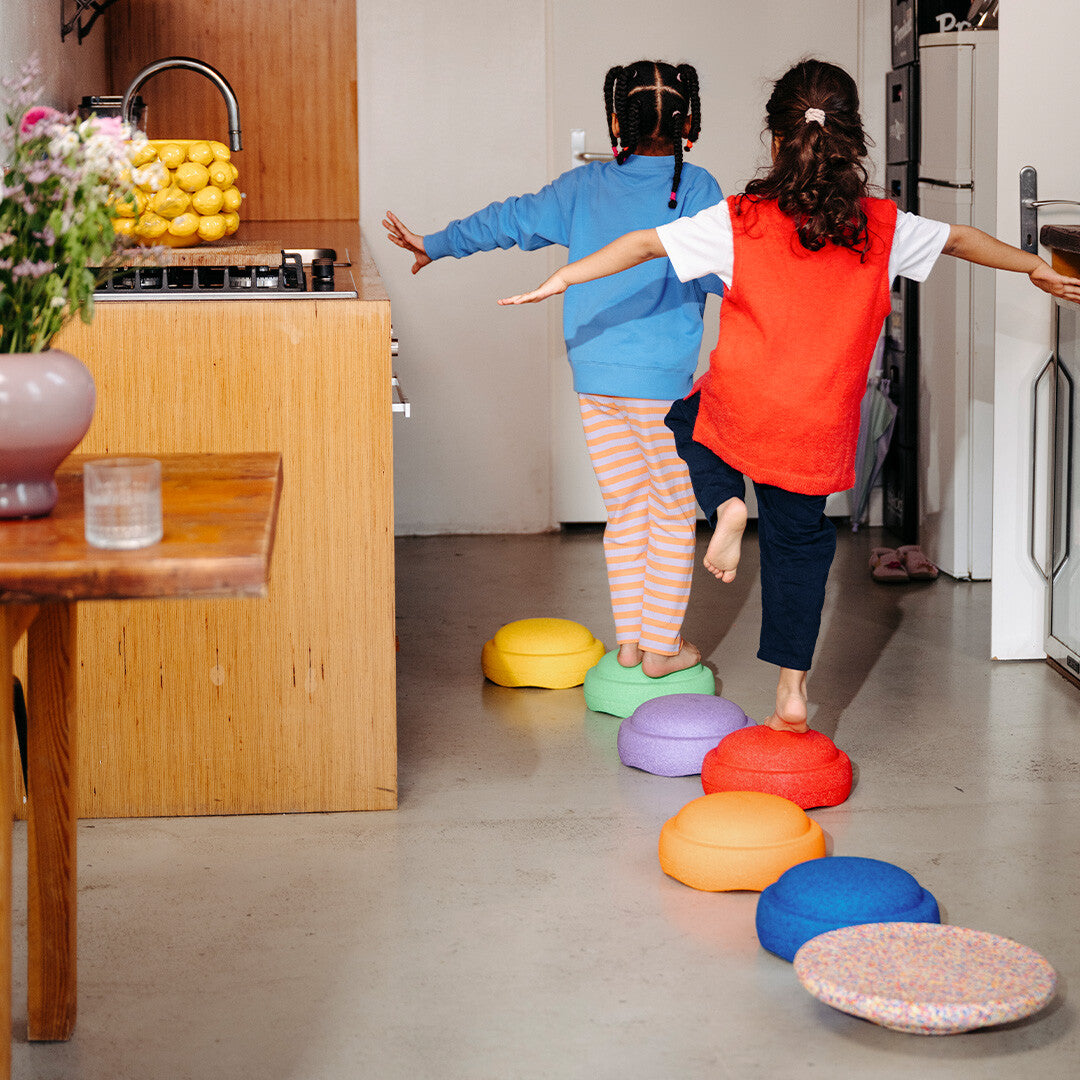Twee kinderen balanceren op stapelstein balance boards die in een rij op de vloer liggen.