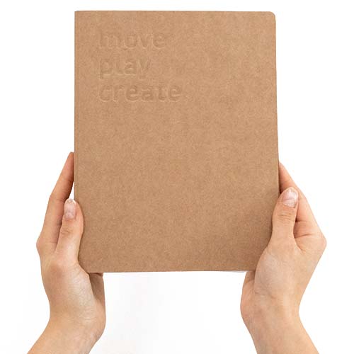 Twee handen houden het stapelstein spellenboek met de tekst 'move play create' op de bruine kaft.