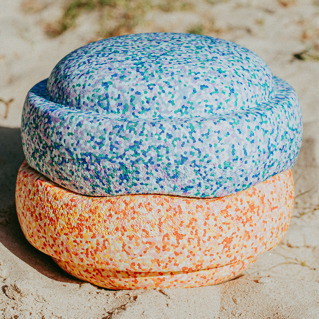Twee grote stapelspeelgoed elementen in pastelkleuren liggen op elkaar in het zand.