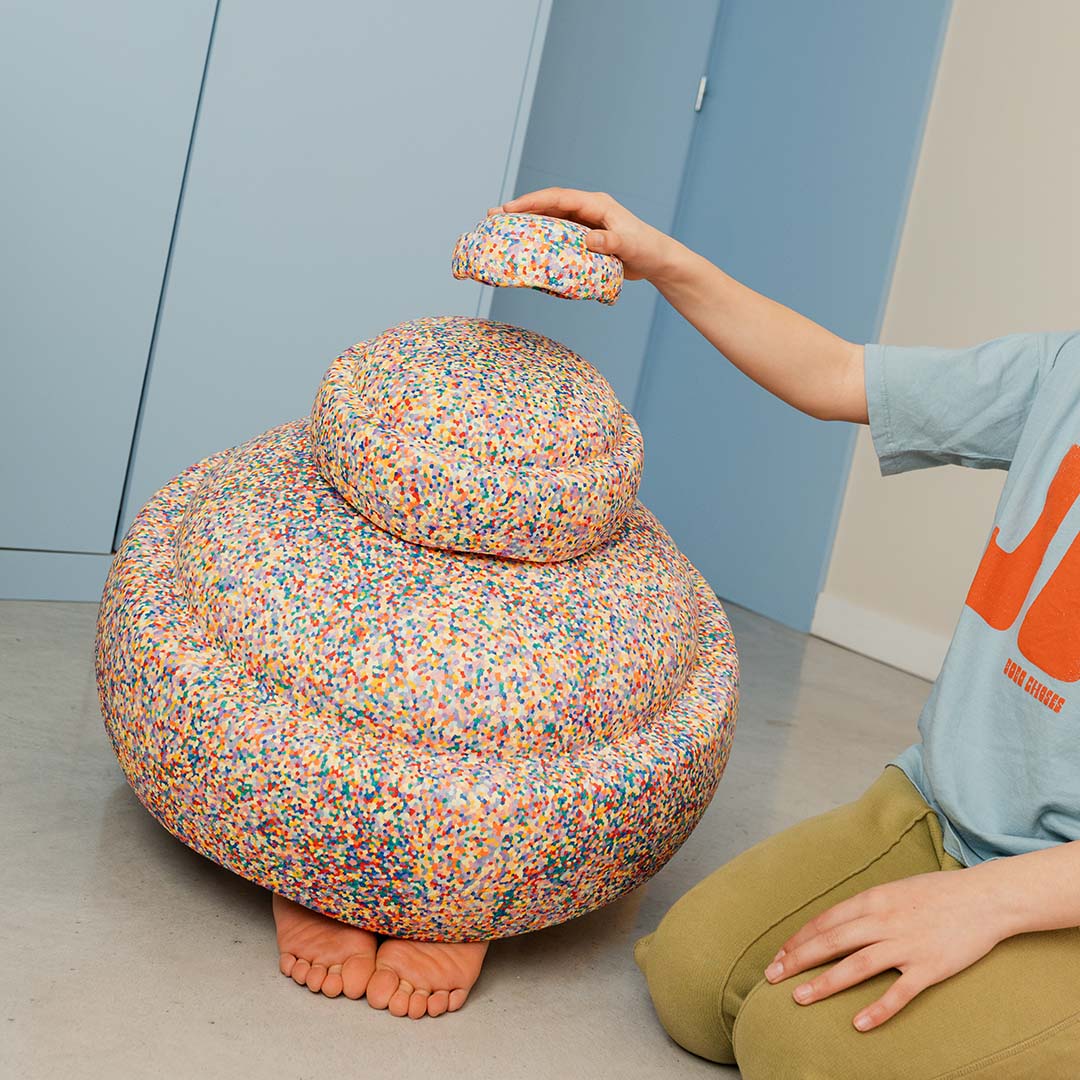 Een kind plaatst het kleinste Stapelstein schuimrubberblok met confetti patroon op twee gestapelde blokken.