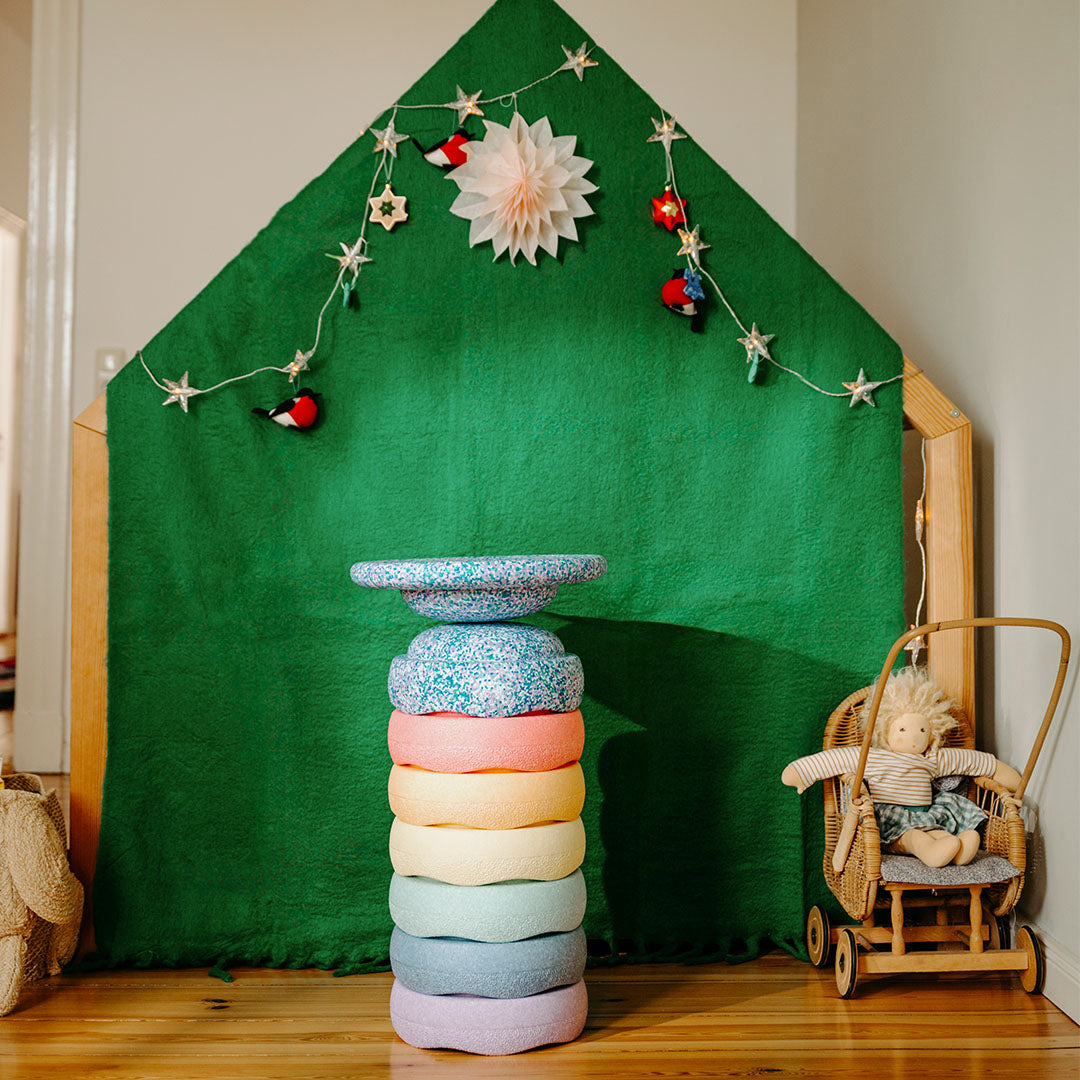 Een stapel stapelstein schuimrubberblokken in pastel regenboogkleuren staat in een kamer met een groen speelhuisje.