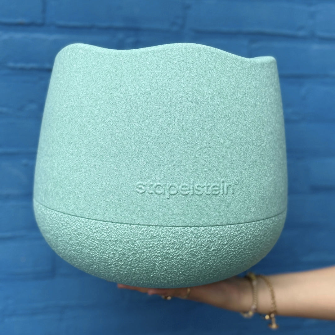 Een hand houdt de stapelstein lichtgroene base, een bouwspeelgoed element, voor een blauwe muur.