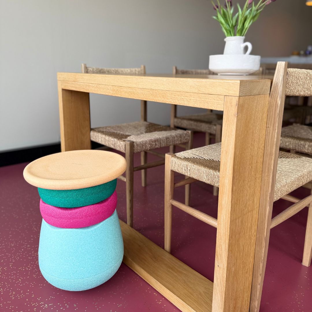 Stapelstein stapelblokken in lichtblauw, roze, groen en lichtbruin, gestapeld als krukje naast een houten tafel met stoelen.