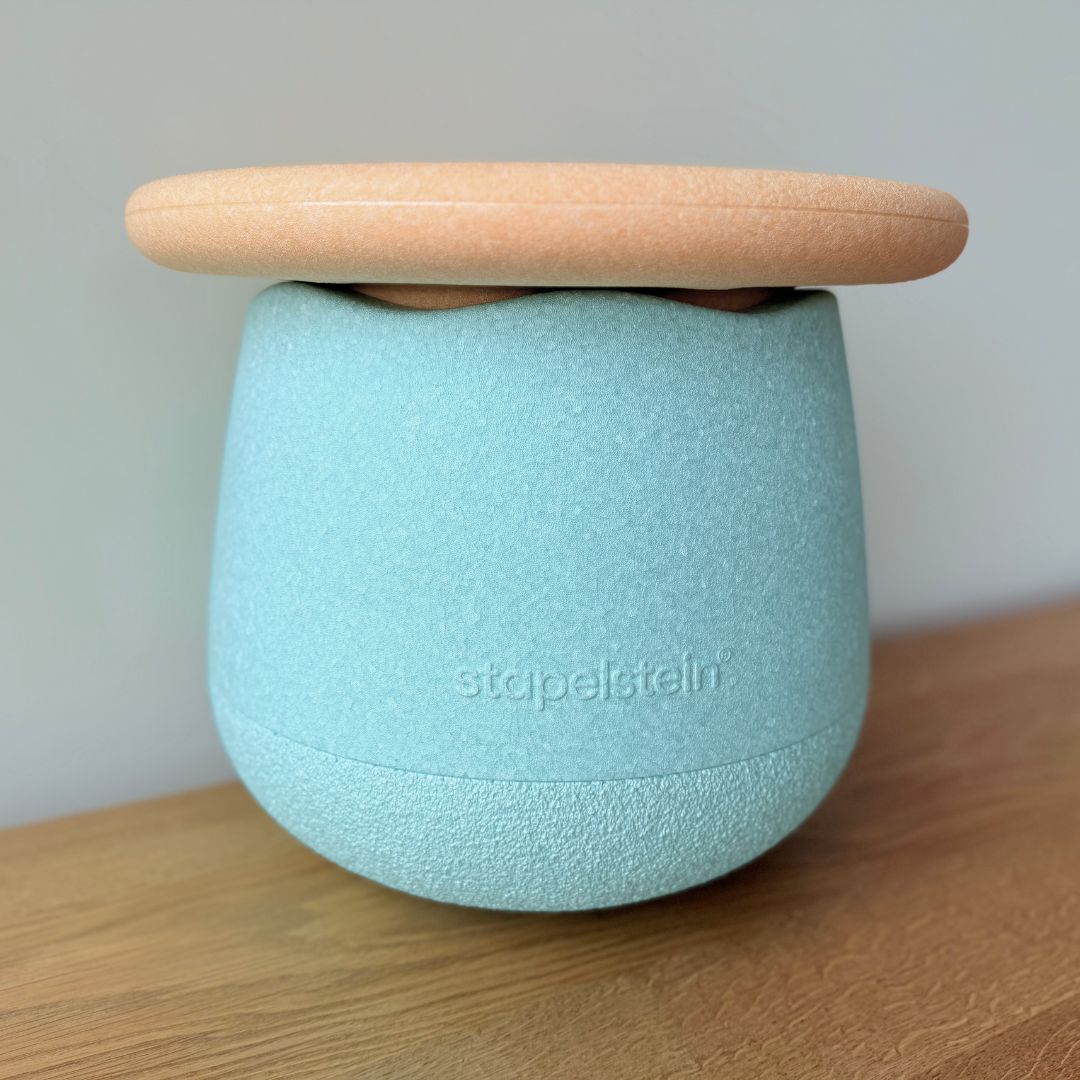 Het Stapelstein dynamic small fitnessspeeltje met lichtblauwe basis en oranje bovenkant staat op een houten ondergrond.