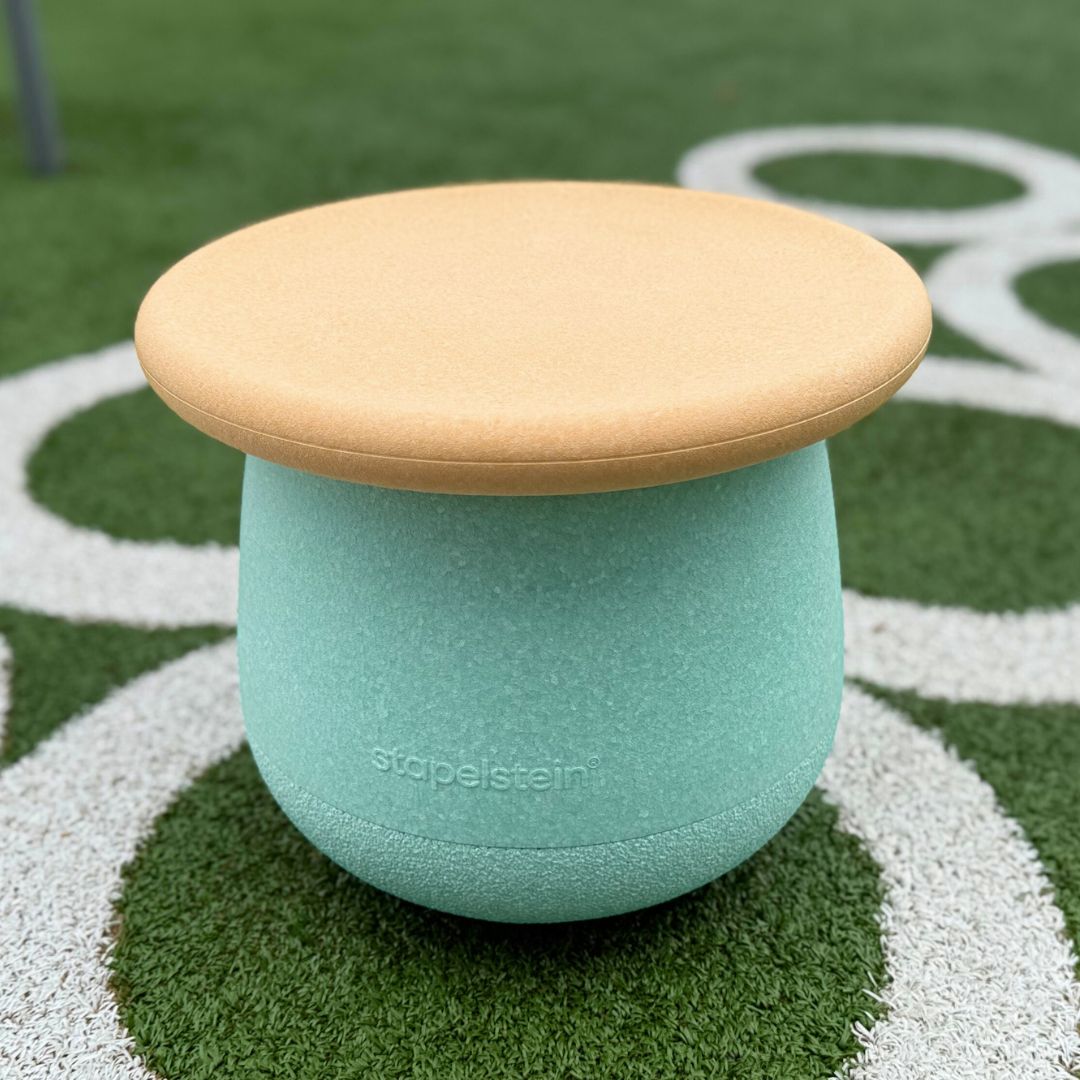 Het Stapelstein dynamic small fitnessspeeltje met lichtblauwe basis en oranje bovenkant staat op groen kunstgras.