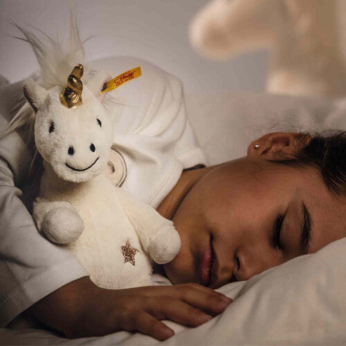 Een slapend kind knuffelt de Steiff pluchen eenhoorn in bed.