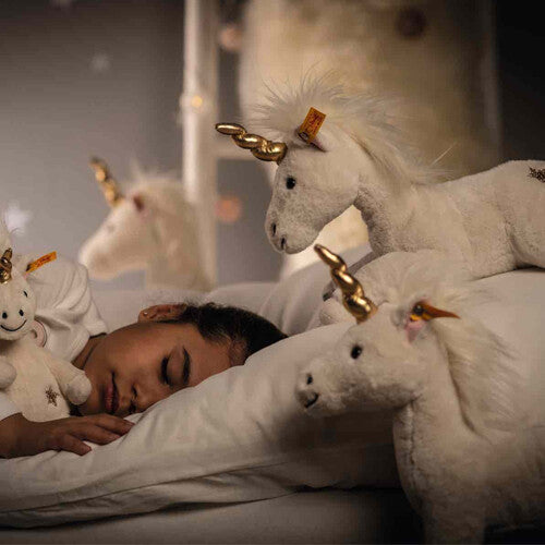 Een kind slaapt in bed met twee Steiff pluchen eenhoorns naast zich.