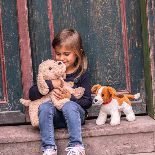 Een meisje knuffelt de Steiff pluchen Goldendoodle Berno hond, met een andere pluchen hond ernaast.