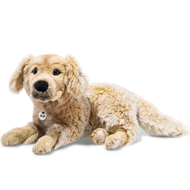 Steiff knuffelhond Andor, een beige pluchen hond, ligt schuin op de grond.