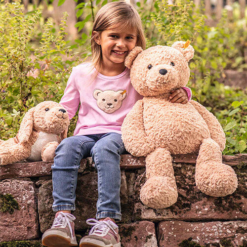 Een meisje zit buiten op een muurtje met de Steiff teddybeer Jimmy en een pluchen hond.