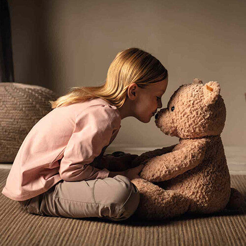 Een meisje kust de neus van de Steiff teddybeer Jimmy.