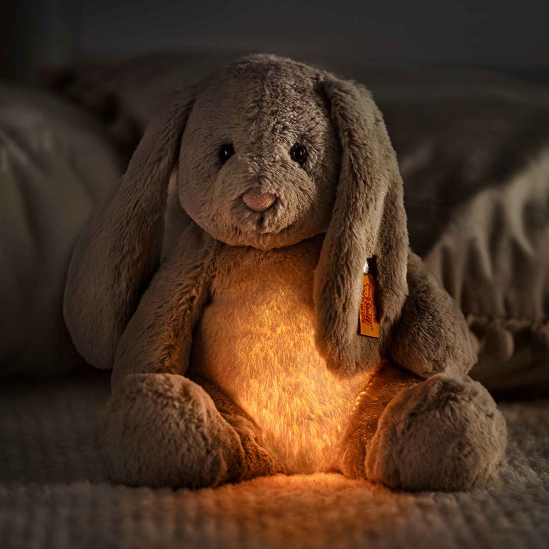 Steiff pluchen knuffelkonijn Hoppi met een warm oranje gloeiend nachtlampje in zijn buik, zittend in het donker.