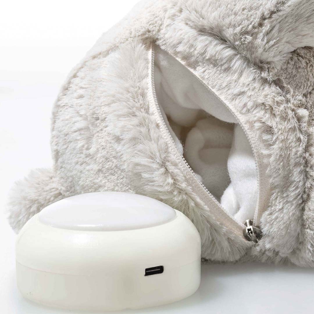 Detailfoto van de open rits op de rug van het pluchen konijn, met ernaast de witte oplaadbare lichtmodule van het nachtlampje.