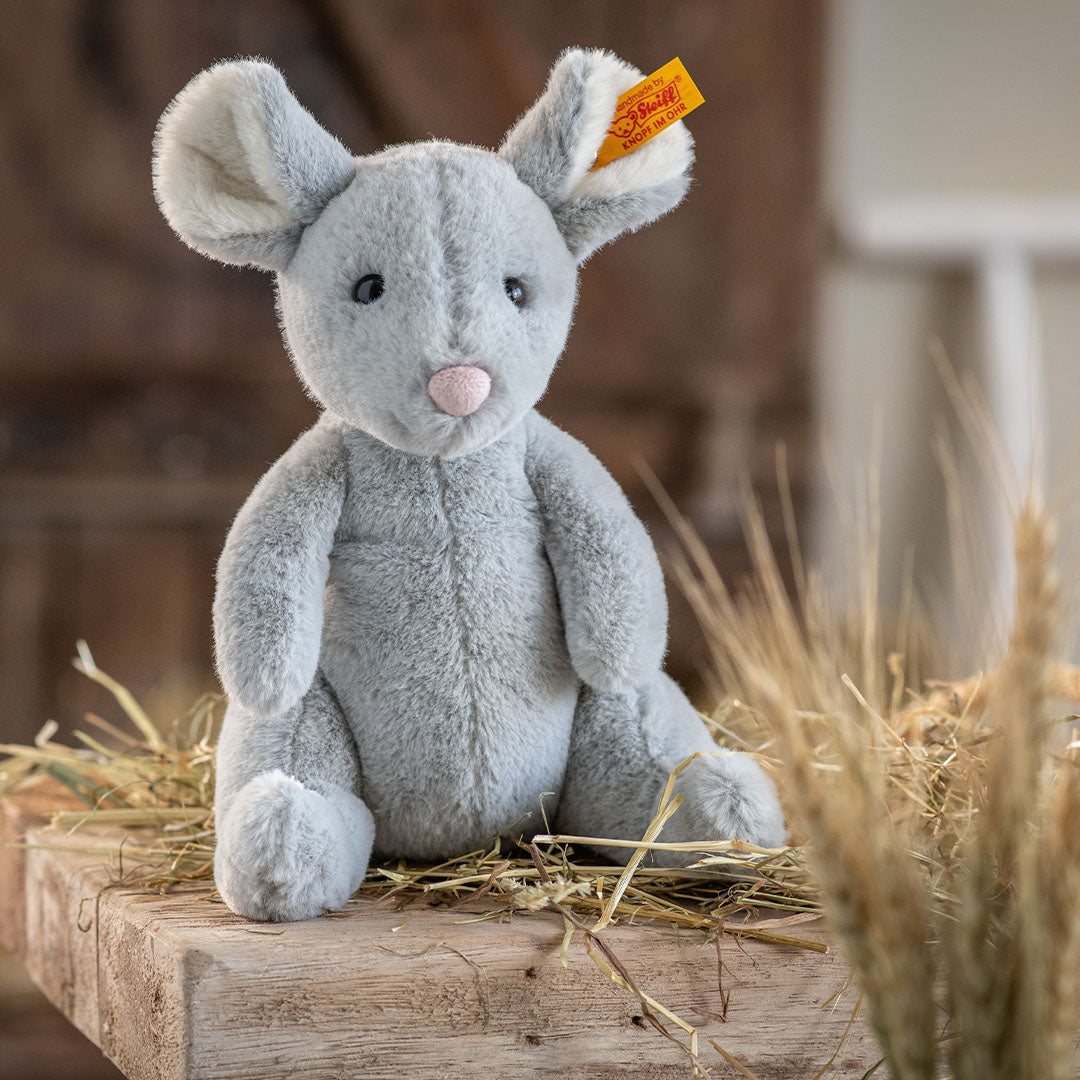 Steiff knuffelmuisje Cheesy, grijs, zit op een houten plank met stro.