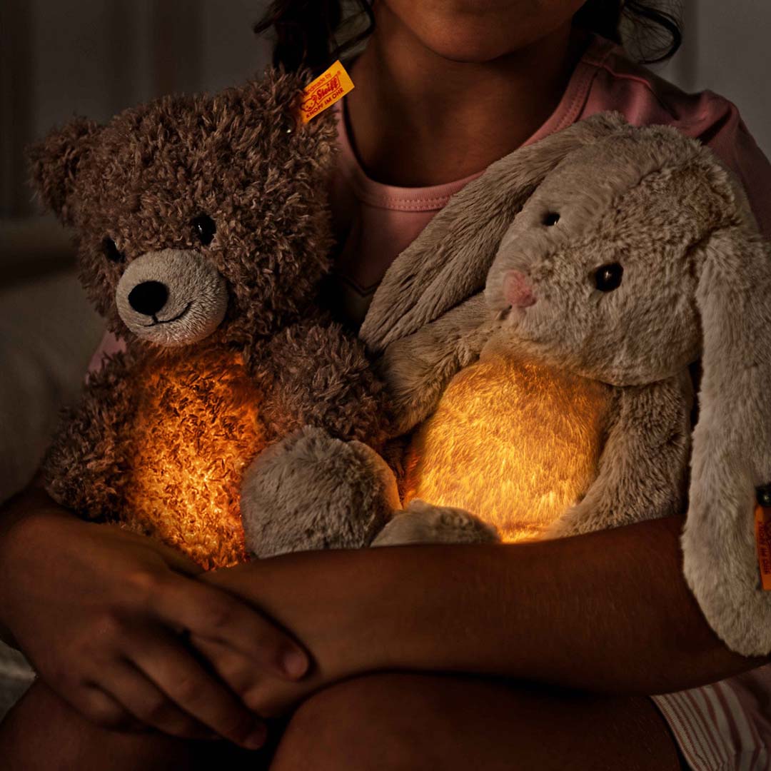 Een kind dat een oplichtende Steiff teddybeer en een oplichtend pluchen konijn vasthoudt.