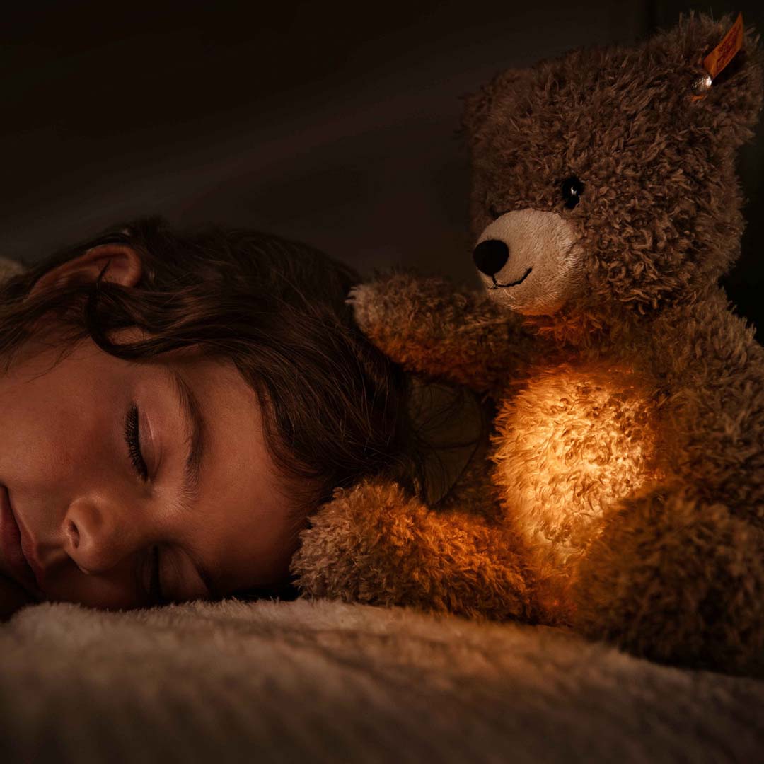 Een slapend kind met een oplichtende Steiff teddybeer als nachtlampje naast zich.