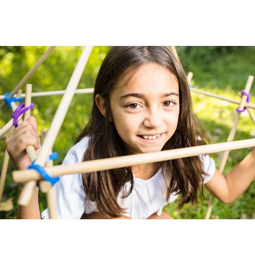 Een lachend meisje bouwt een constructie van houten stokken met veelkleurige stick-lets connectors.
