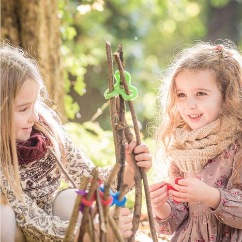 Twee meisjes bouwen een constructie van takken met veelkleurige stick-lets connectors in het bos.