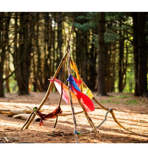 Een gebouwde hut van takken en kleurrijke stoffen in het bos, verbonden met stick-lets connectors.