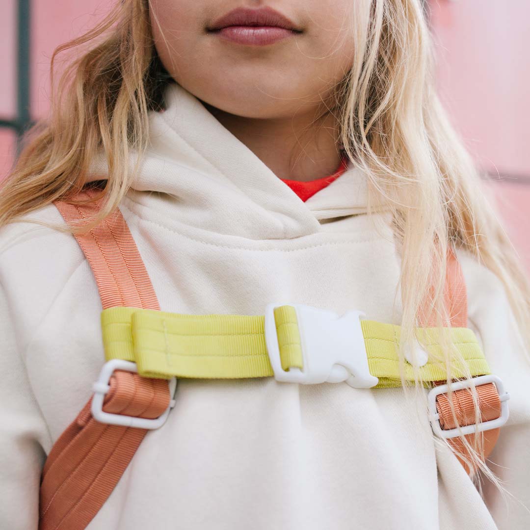 Kind draagt een gele sticky lemon borstriem voor rugzak over een witte hoodie.