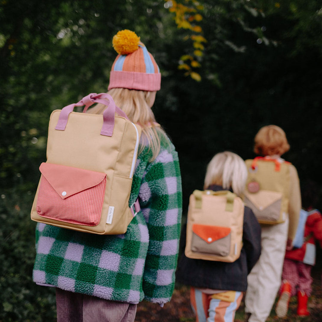 Drie kinderen lopen in een bos met verschillende Sticky Lemon schoolrugzakken op hun rug.