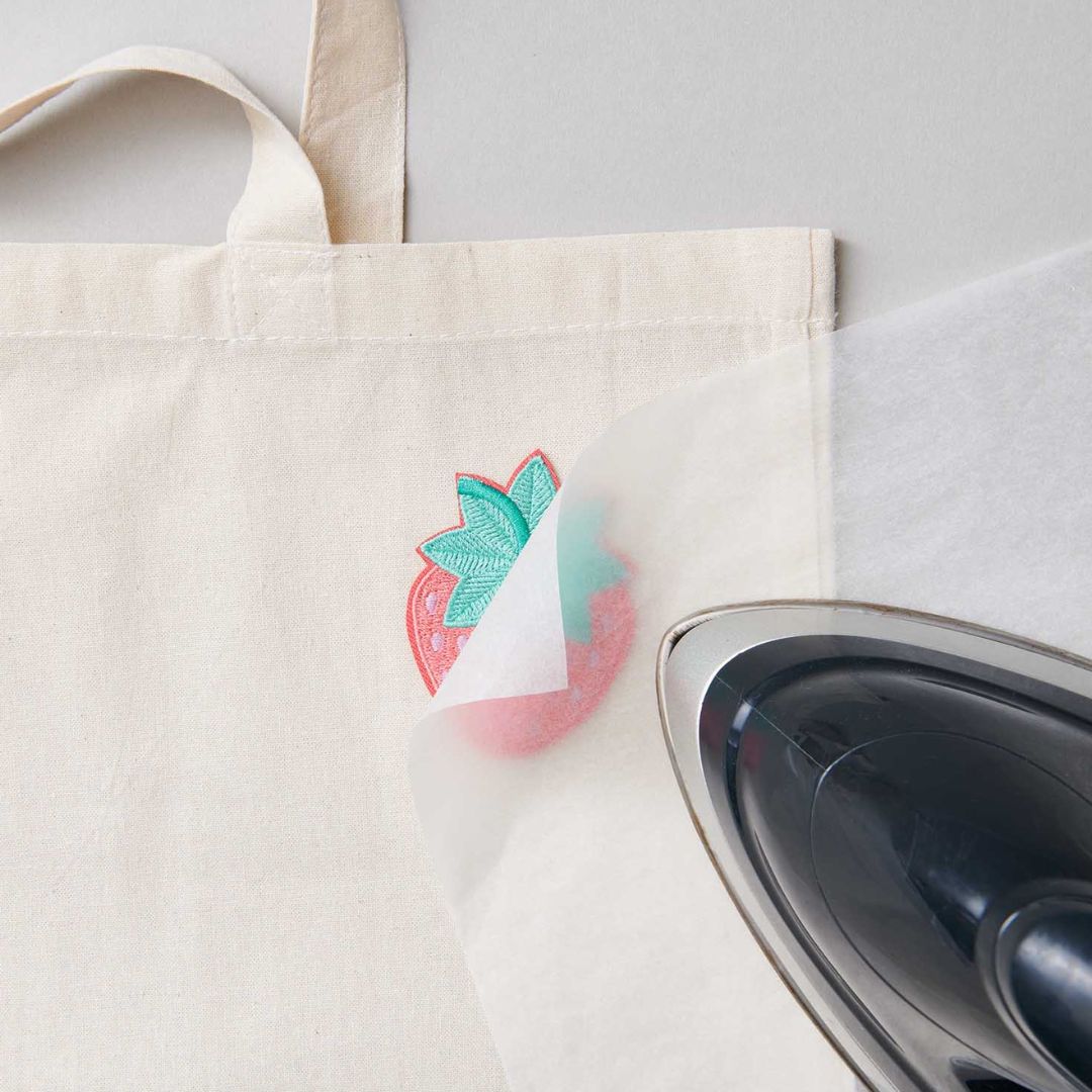 Een strijkijzer bevestigt de aardbei strijkpatch op een stoffen tas.