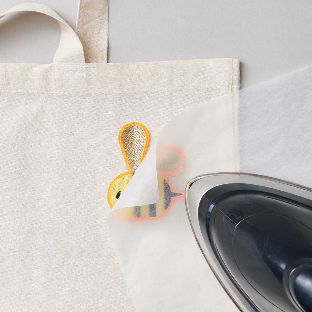 Een strijkijzer dat een bij opstrijkpatch op een stoffen tas bevestigt, met een beschermvel dat wordt verwijderd.