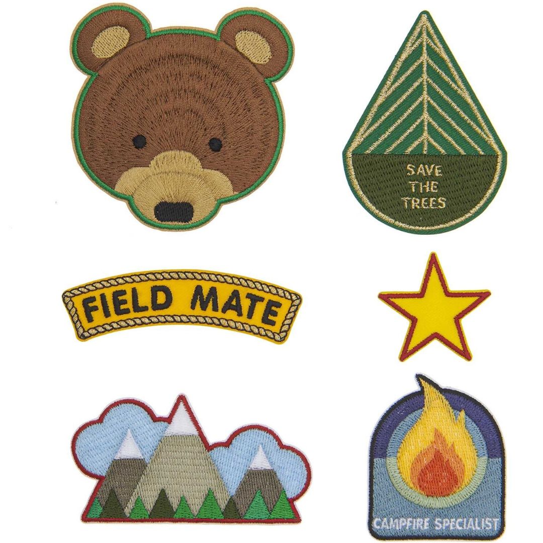 Rico Design set van zes veelkleurige opstrijkpatches met scoutingthema, waaronder een beer, boom, bergen en kampvuur.