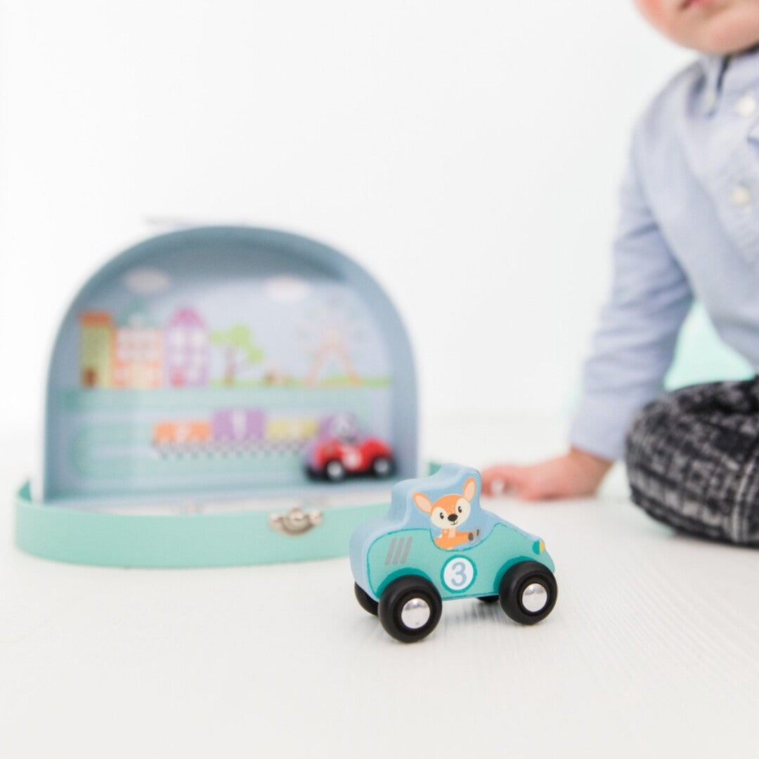 Detail van een lichtblauwe Studio Circus houten raceauto met een hertje en nummer 3, met de speelgoedkoffer op de achtergrond.