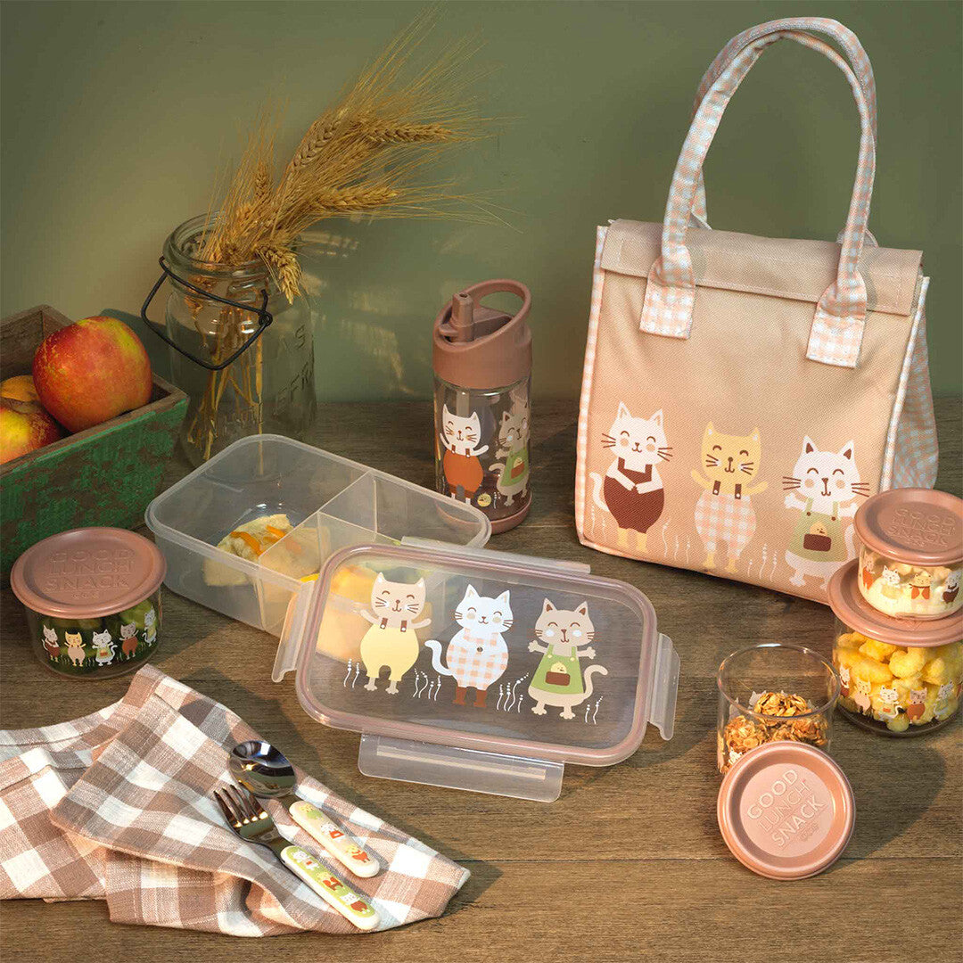 Collectie van sugarbooger lunchartikelen voor kinderen met kattenprint, inclusief bento lunchbox, lunchtas en drinkfles, op een houten tafel.