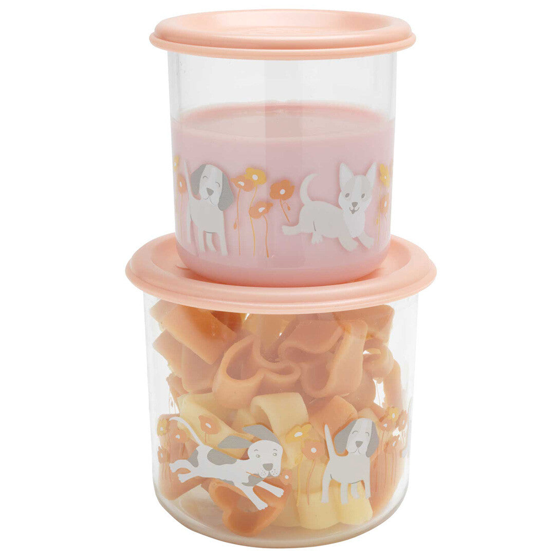 Twee gestapelde plastic snackdoosjes met roze deksels, gevuld met roze vloeistof en oranje pasta, met een patroon van puppies en bloemen.