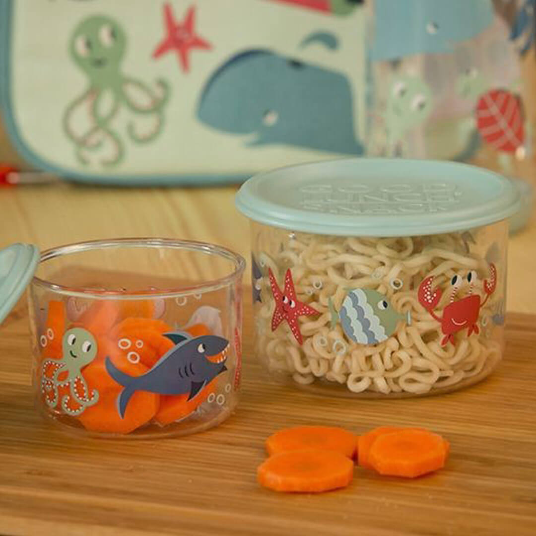 Sugarbooger plastic snackdoosjes met oceaan dieren, gevuld met wortels en noodles op een houten ondergrond.