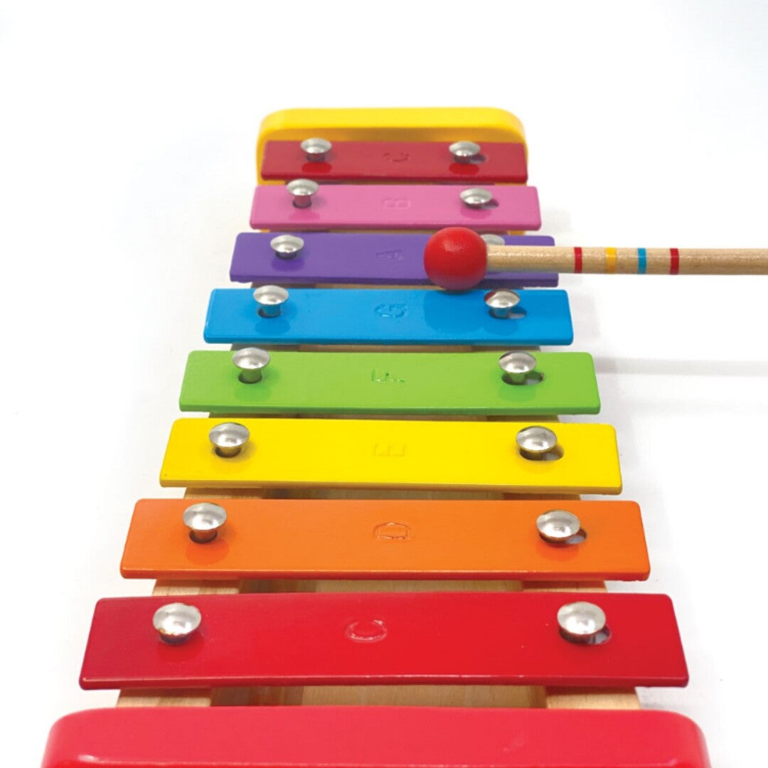 Bovenaanzicht van de regenboog xylofoon met een rode mallet die een paarse staaf raakt.