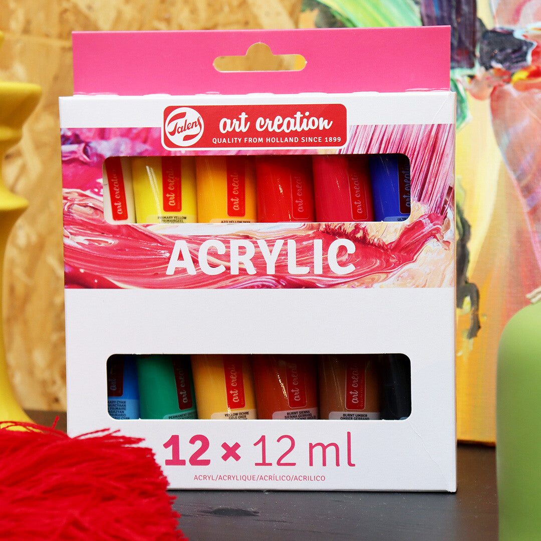 De verpakking van Talens Art Creation acrylverf met 12 tubes, staand op een tafel met kunstbenodigdheden.