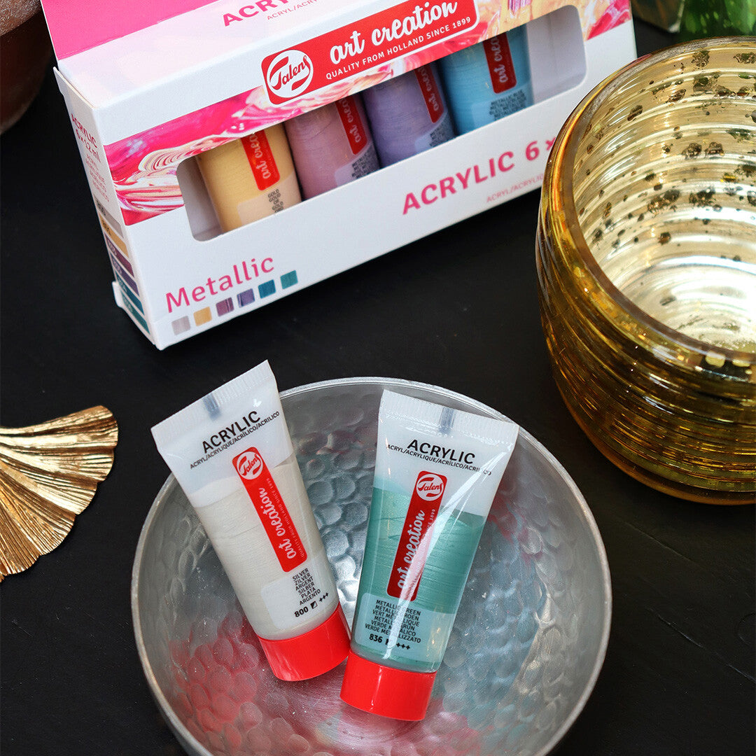 Twee tubes Talens Art Creation metallic acrylverf in een schaal met de verpakking op de achtergrond.