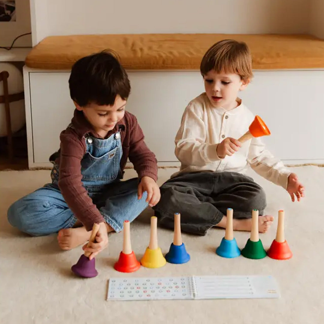 Twee kinderen spelen met de tambu Ding Dang Bú regenboog handbellen en een muziekboekje op de grond.