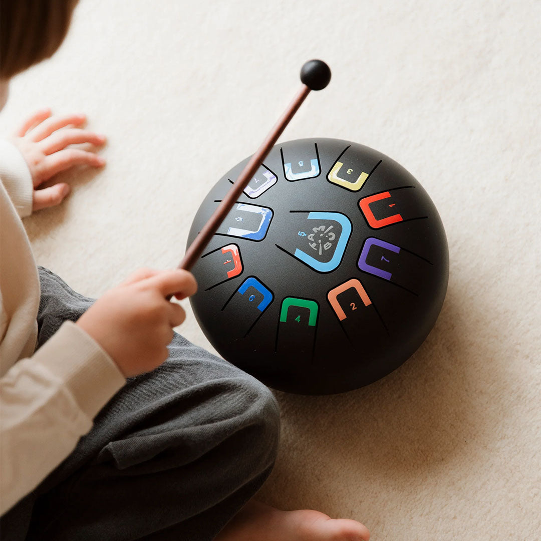 Een kind speelt met een tambu tongtrommel met een mallet.