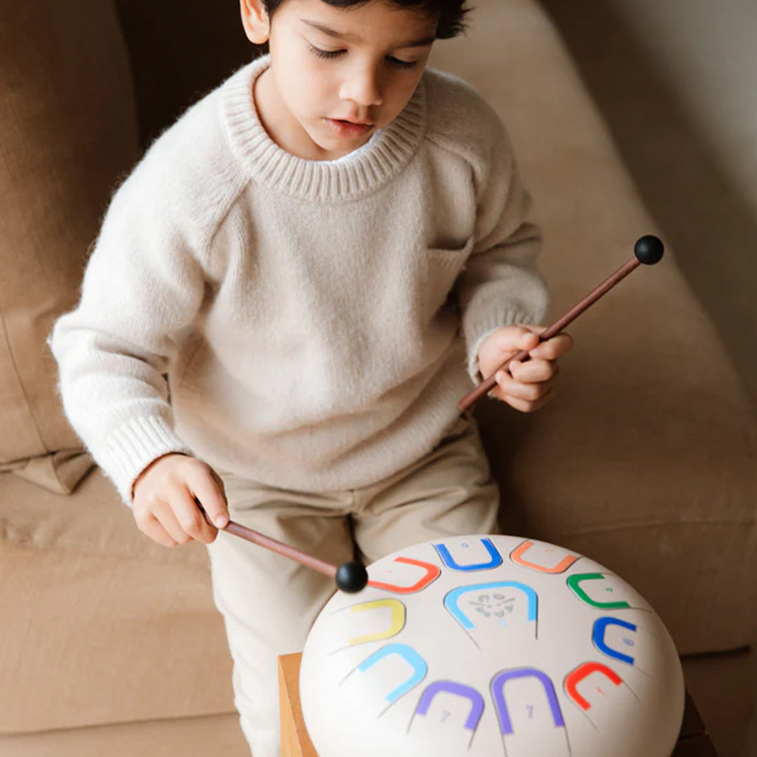 Een kind speelt op de beige tambu tongtrommel met twee mallets.