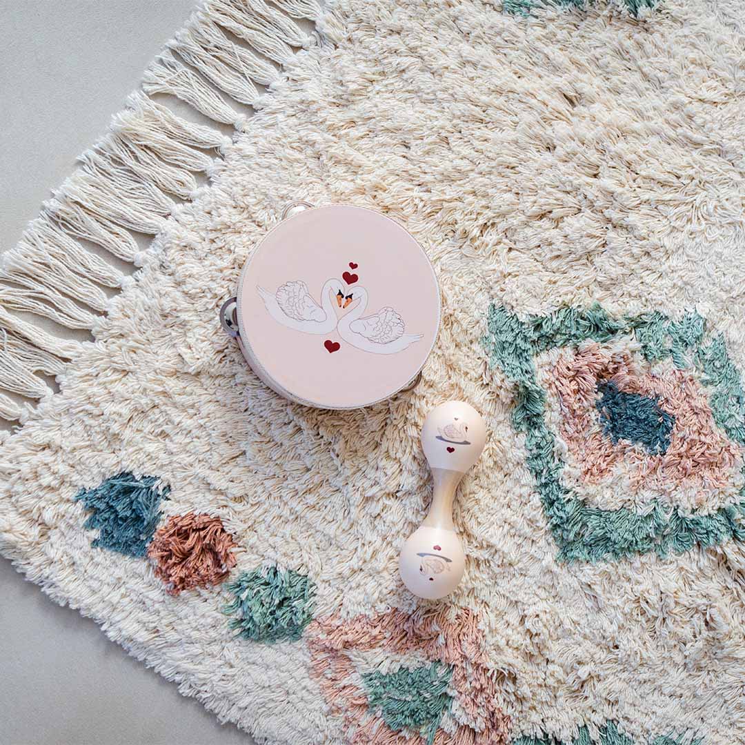 Detail van het Tapis Petit vloerkleed met diamantpatroon en franjes, met een rammelaar en tamboerijn erop.