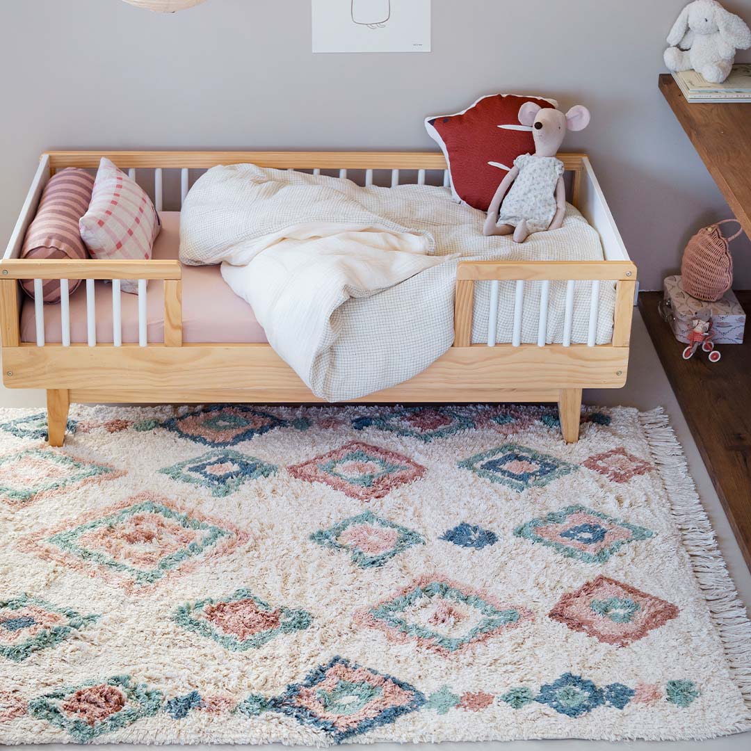 Tapis Petit vloerkleed met diamantpatroon ligt op de vloer onder een houten kinderbed.