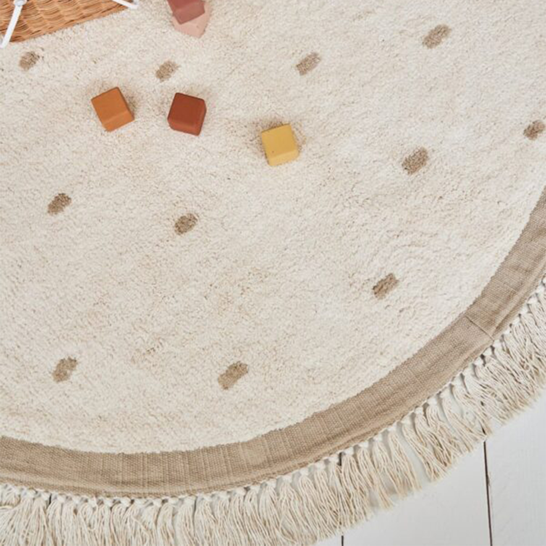 Detailopname van het tapis petit vloerkleed Puck met stippen en franjes, met houten speelblokken erop.