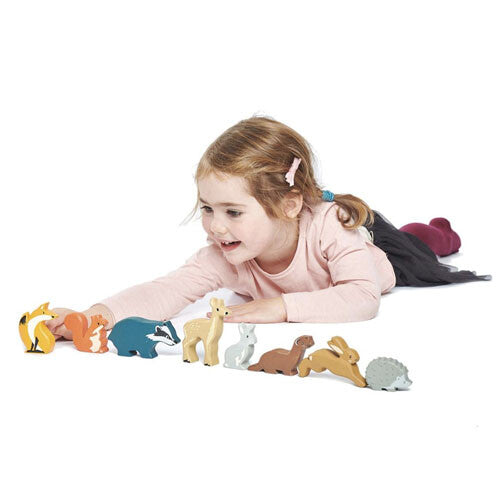 Een meisje speelt met de houten bosdierenfiguurtjes op de grond.