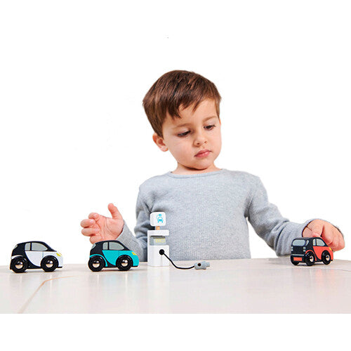 Een jongen speelt met de Tender Leaf Toys houten elektrische auto's en laadpaal op een tafel, waarbij de blauwe auto is aangesloten.