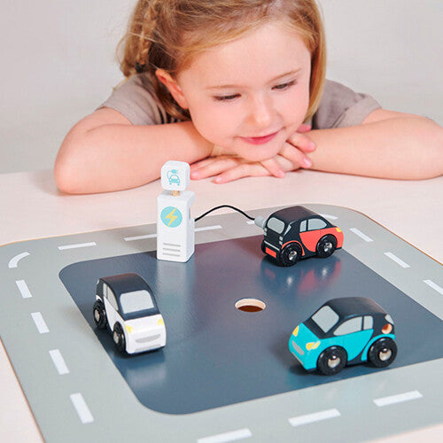 Een meisje speelt met de Tender Leaf Toys houten elektrische auto's en laadpaal op een speelmat met wegen.